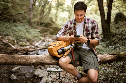 Handsome hiker using phone in a forest while taking a little break