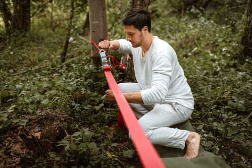 Young man preparing slackline for a balancing workout in a forest