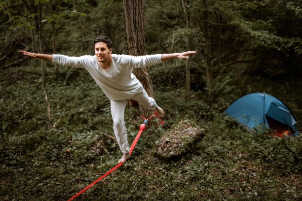 Young man balancing on a slackline in a forest in front of his camping tent
