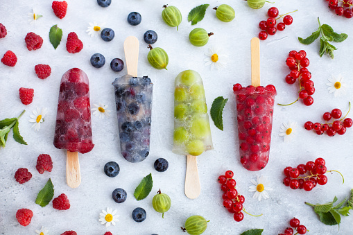 Four frozen ice cream popsicles with raspberries, gooseberries, blueberries and red currants. Healthy food. Summertime wallpaper. Top view, flat lay.