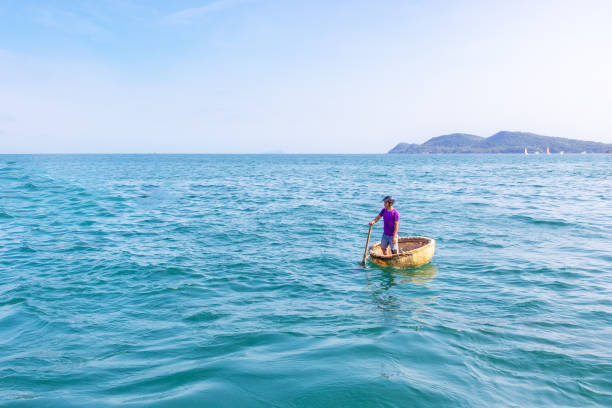 Vietnamese fisherman with his basket boat Phu Quoc island, Vietnam - March 21, 2019: Alone vietnamese fisherman with his round bamboo basket boat in open sea basket boat stock pictures, royalty-free photos & images