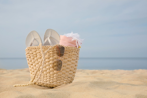 Beach bag with flip flops, towel and sunglasses on sandy seashore, space for text