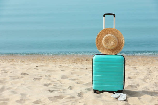 istock Turquoise suitcase, flip flops and straw hat on sandy beach, space for text 1397927088