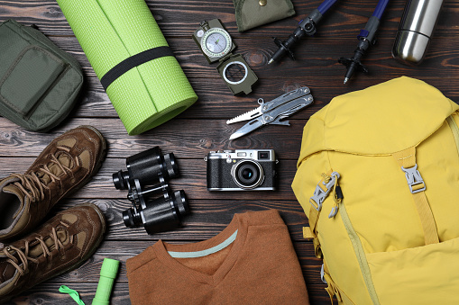 Flat lay composition with backpack and other camping equipment for tourism on wooden background
