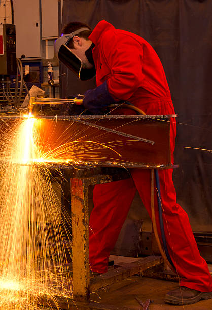 Welder in red overalls cuts metal.