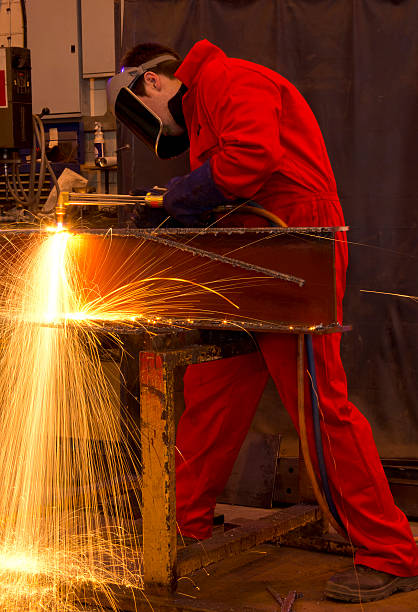 Welder in red overalls cuts metal. Welder in workshop manufacturing metal construction by cutting to shape. oxyacetylene stock pictures, royalty-free photos & images