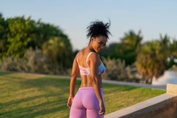 Average aged Afro-Latin woman in her 30s dressed in sportswear is outdoors doing physical exercises to get fit on the stairs of a public park as she looks up at the camera