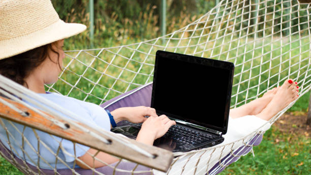 istock Back view young woman in summer hat student typing using laptop for e learning distance training course, lying on hammock outdoors. Working online at home. Over shoulder close up mock up screen view 1397932148