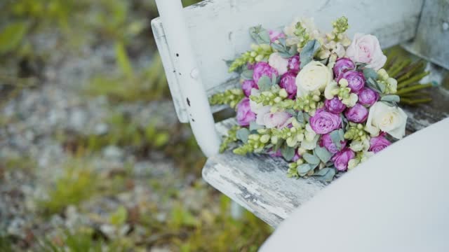 Wedding bouquet of roses lies near dress and sways on old white wooden swing