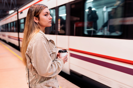 Stock photo of pretty young girl standing in the train platform holding a cup of coffee.