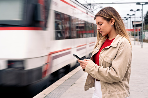 Stock photo of pretty young girl waiting in the train platform using her phone.