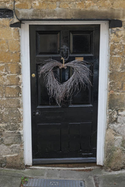 vieille porte noire vintage avec un arrangement décoratif en cœur de brindilles suspendues au heurtoir à l’entrée d’une maison de ville en pierre de cotswold dans la ville romaine historique de cirencester, gloucestershire, angleterre. - doorstep door knocker door england photos et images de collection