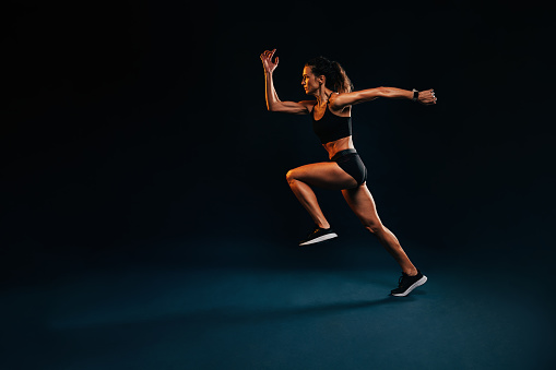 Muscular healthy woman running. Caucasian female runner in sportswear sprinting on black background.