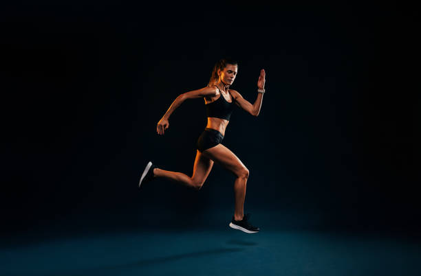 istock Female runner sprinting on black background. Fit woman jumping while exercising in studio. 1397936058