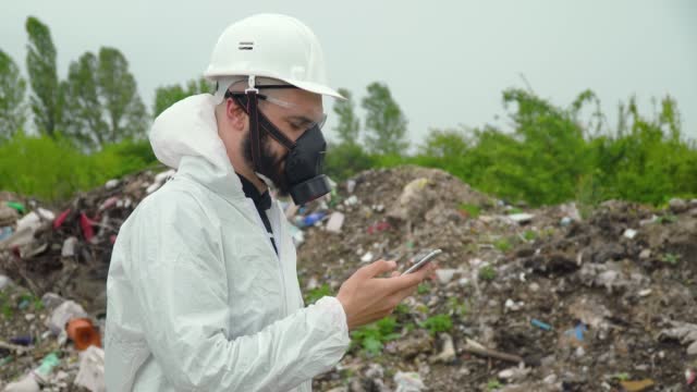 Activist scientist with protective mask is talking on the phone on landfill. Environmental pollution concept
