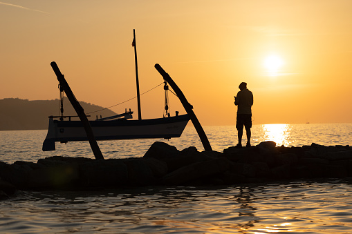 Idylic view of sunset, boat, sea and silhouette of man on coastline.