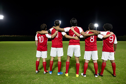 Rear view of a team of soccer players hugging and looking at the field - sports concepts