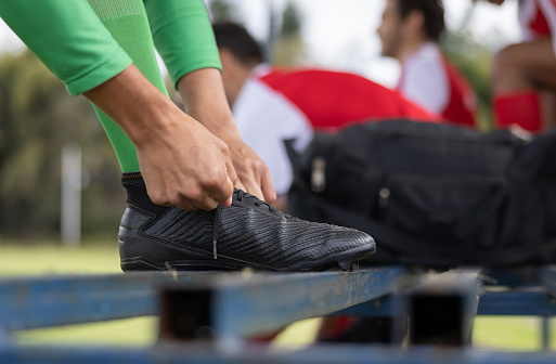 Close-up on a soccer player tying his shoelace on the bench before going in the field - sports concepts
