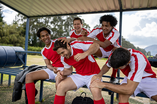 Happy group of Latin American soccer players teasing a teammate and laughing in the bench - sports concepts