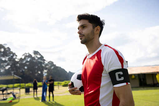Jugador de fútbol con una banda de capitán y sosteniendo una pelota de fútbol en el campo photo