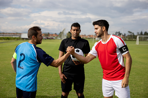 Soccer team captains handshaking in the middle of the field in front of the referee - fairplay concepts