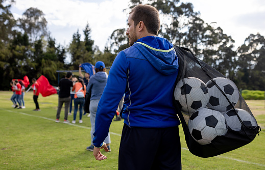 Coach carrying a mesh bag with soccer balls at the end of the practice