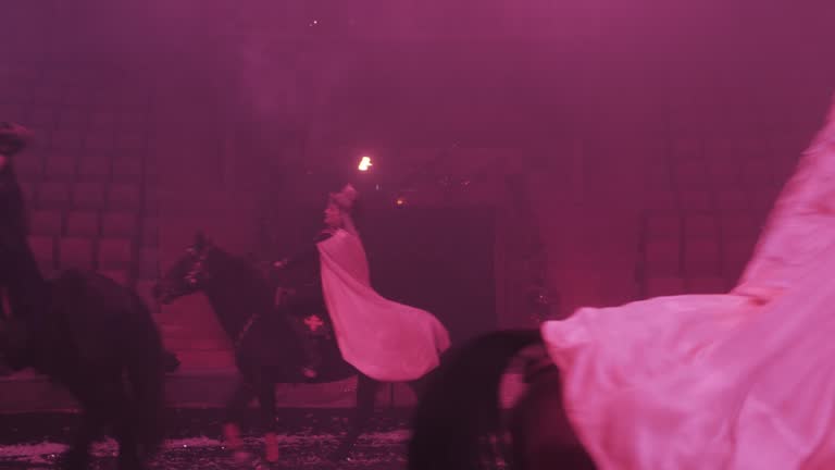 Riders on horseback pass through the circus arena, holding torches in their hands, raincoats fluttering, performance