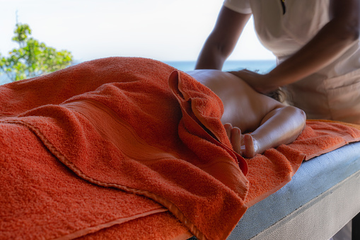 Relaxed woman lying down getting massage therapy in Caribbean beach spa with copy space