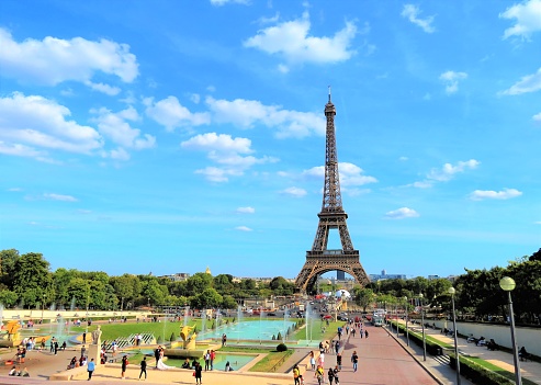 June 9, 2018 - Paris, France. A wide angle view of the Eiffel tower in Paris on a blue sky day with people walking through the park.