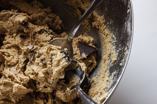an above view of a silver mixing bowl full of chocolate chip cookie dough with two silver spoon for scooping