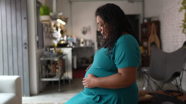 Pregnant woman touching her belly and contemplating at home