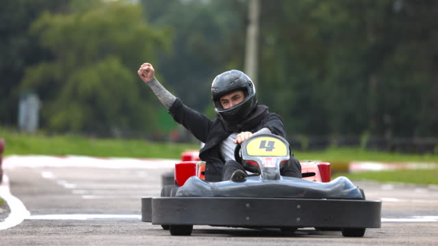 Latin American man celebrating he won at a go-cart racing track with arms raised