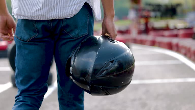 Unrecognizable back view of man holding a sports helmet while walking towards a go-cart at the track
