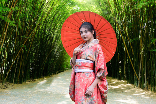 A woman in a kimmono dress holds an umbrella in a bamboo grove in Japan. Major tourist attractions in Japan