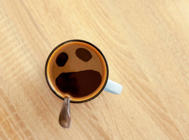 Coffee cup with funny screaming in fear face, top view. Open crying mouth in mug on table background. Shocked, stressed, angry, scared and furious foam emoticon head. Pareidolia effect at breakfast