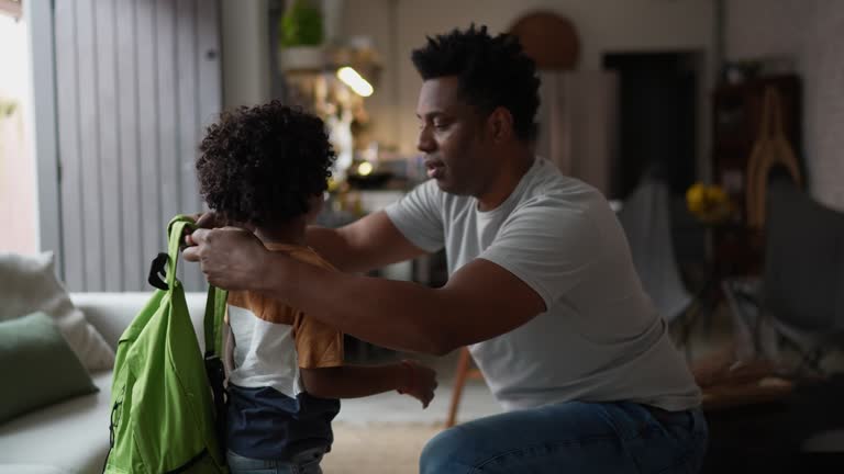 Father helping son with backpack at home before leaving to school