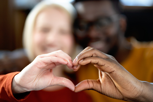 Multi-ethnic couple showing a heart symbol made by their hands