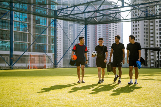 footballeurs asiatiques souriants marchant sur un terrain de sport pour s’entraîner - foot walk photos et images de collection