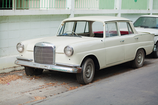 White colored Mercedes oldtimer parked in Bangkok Ladprao. Car is damaged and has some windows and the star missing