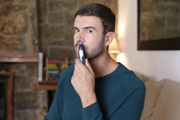 homme utilisant une tondeuse à poils de nez à la maison - mature adult home interior chair contemporary photos et images de collection