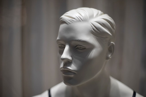 Mannequin face. White figure made of plastic. Details of showcase of clothing salon. Light and shadow on head of sculpture.