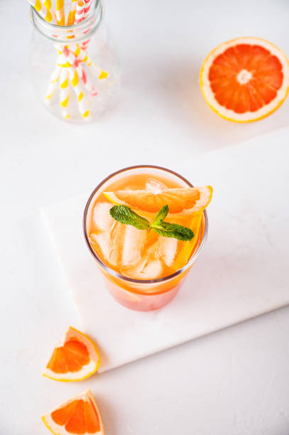 istock Fresh grapefruit juice with ice, mint and grapefruit slice in a glass on a white marble background with citrus  slices and paper tubes. Top view 1397957375