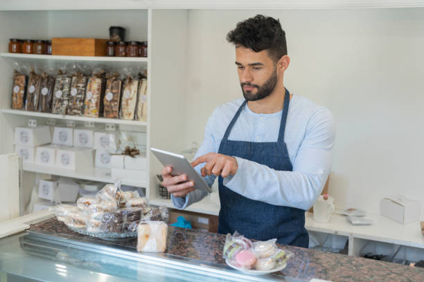 Entrepreneur  using a digital tablet at patisserie An employee is using a digital tablet at patisserie point of sale tablet stock pictures, royalty-free photos & images