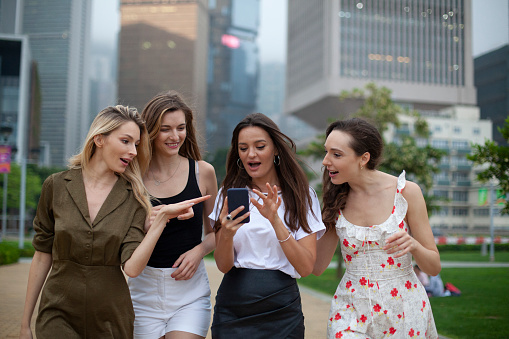 Happy women walking in the city and having fun with smart phone