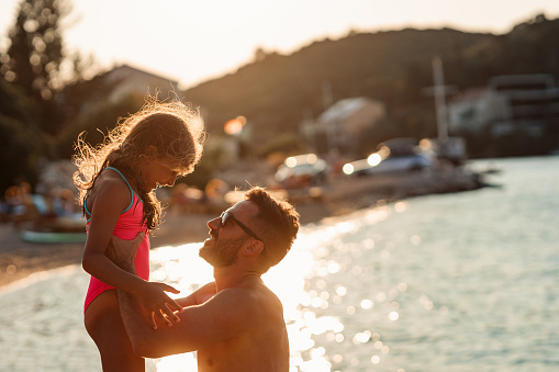 Young man spending time at the beach with his adorable daughter and having fun