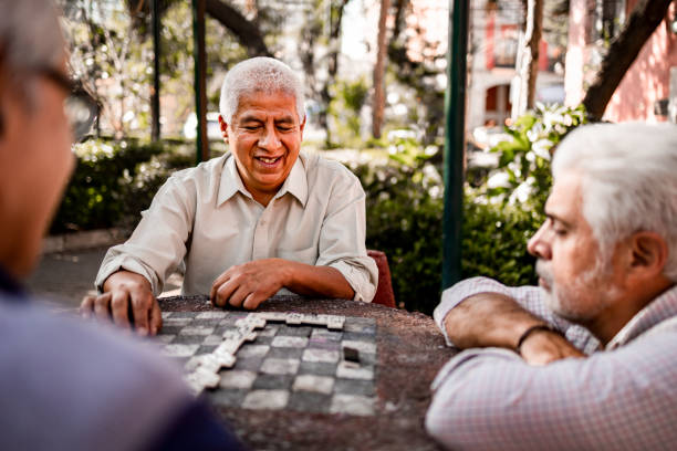 Three senior men sitting in the park and playing domino stock photo