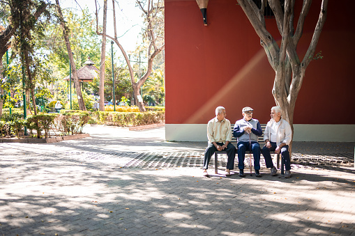 Three senior friends sitting in the bench in front of the building