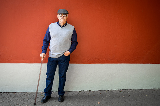 Portrait of a senior man leaning on the wall. He is holding walking can