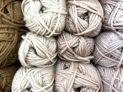 Horizontal closeup photo of rows of multi colored balls of wool stacked on top of each other, in a row,  on a display shelf in a shop.