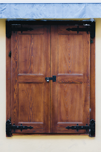 Brown old wooden closed shutters on the facade of the house. Vintage window.